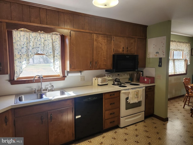 kitchen with light floors, light countertops, a sink, black appliances, and baseboards