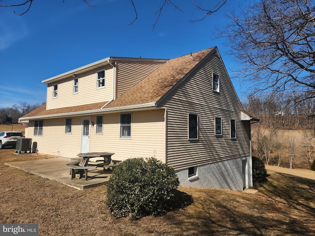 back of house with central air condition unit, a shingled roof, and a patio