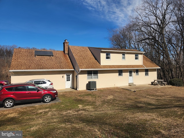 back of house with cooling unit, roof with shingles, a yard, and a chimney