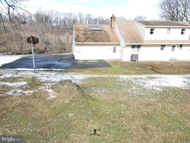 rear view of house with a chimney, aphalt driveway, roof with shingles, cooling unit, and a yard