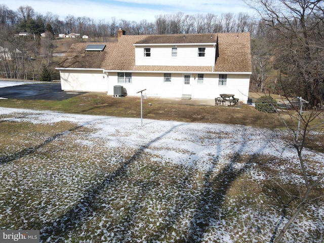 back of house featuring a shingled roof, central AC, a chimney, and aphalt driveway