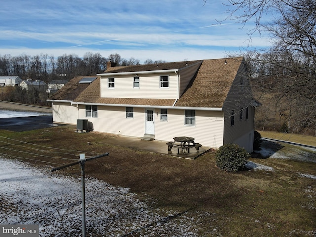 back of house with a patio, central air condition unit, a garage, a shingled roof, and a chimney