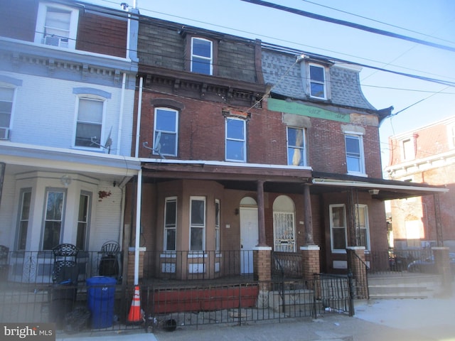 view of front facade with covered porch, mansard roof, roof with shingles, and brick siding