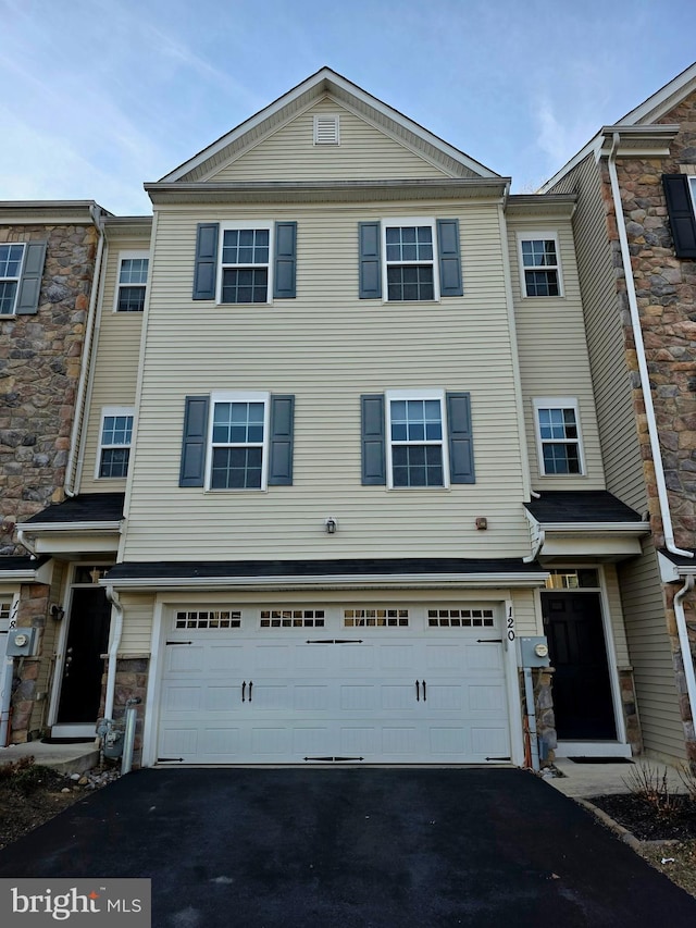 view of property with a garage, stone siding, and aphalt driveway