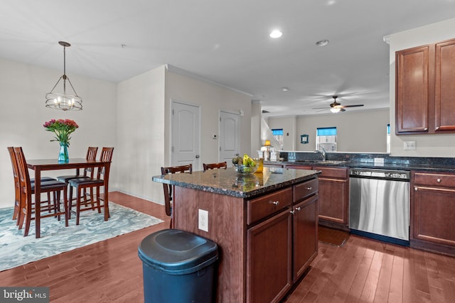 kitchen with a center island, dark wood finished floors, stainless steel dishwasher, a sink, and dark stone countertops