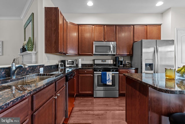 kitchen featuring dark wood-style flooring, crown molding, stainless steel appliances, a sink, and dark stone countertops