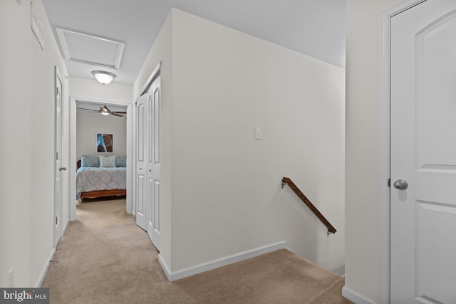 hall featuring light carpet, attic access, baseboards, and an upstairs landing