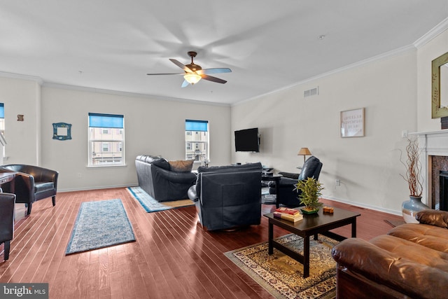 living room featuring a fireplace with raised hearth, wood finished floors, visible vents, baseboards, and ornamental molding