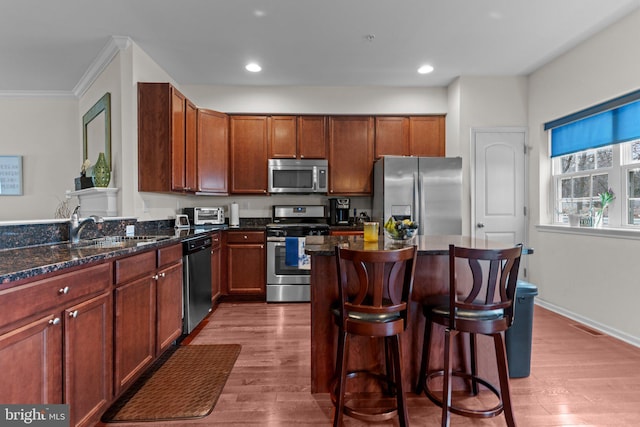 kitchen with stainless steel appliances, wood finished floors, a sink, a kitchen breakfast bar, and dark stone countertops