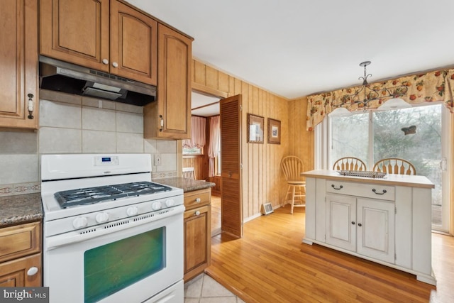 kitchen with decorative light fixtures, tasteful backsplash, light wood-type flooring, under cabinet range hood, and white gas range oven