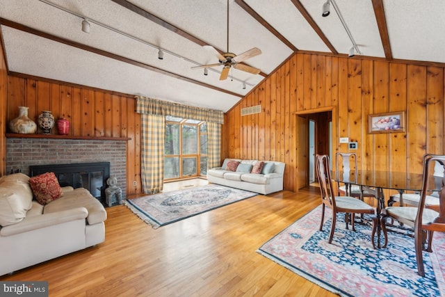 living area featuring lofted ceiling, a brick fireplace, wood finished floors, and wood walls