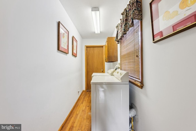 clothes washing area featuring light wood-type flooring, baseboards, cabinet space, and washing machine and clothes dryer