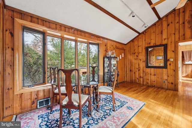 dining room with lofted ceiling, visible vents, and wooden walls