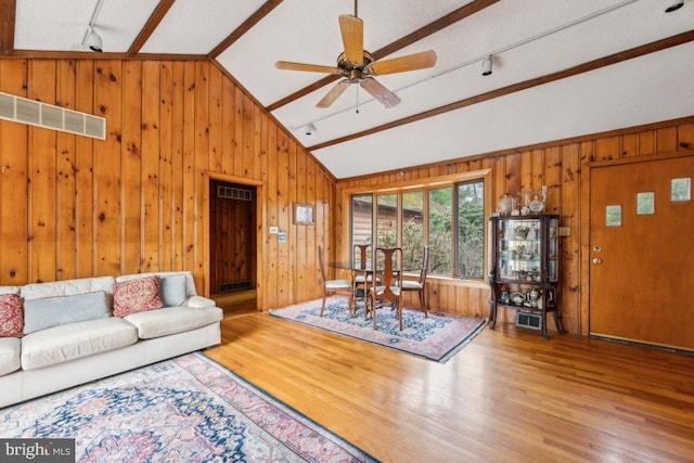 living room featuring a ceiling fan, lofted ceiling, wood walls, and wood finished floors