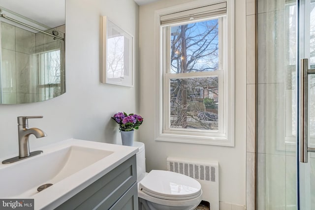 bathroom with a shower with door, vanity, toilet, and radiator heating unit