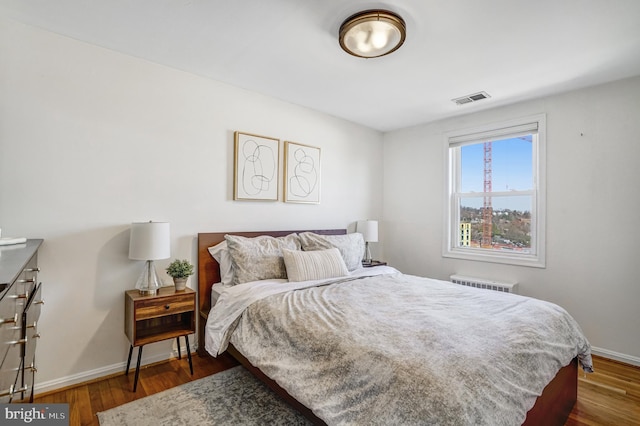 bedroom featuring visible vents, baseboards, wood finished floors, and radiator heating unit