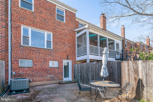 back of house featuring brick siding, fence, central AC unit, a sunroom, and a patio area