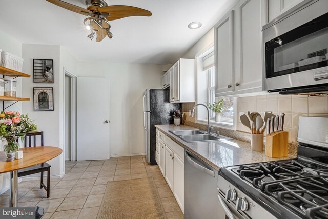 kitchen featuring tasteful backsplash, stainless steel appliances, light tile patterned flooring, white cabinetry, and a sink