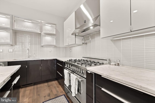 kitchen featuring a sink, white cabinets, wall chimney range hood, backsplash, and stainless steel range