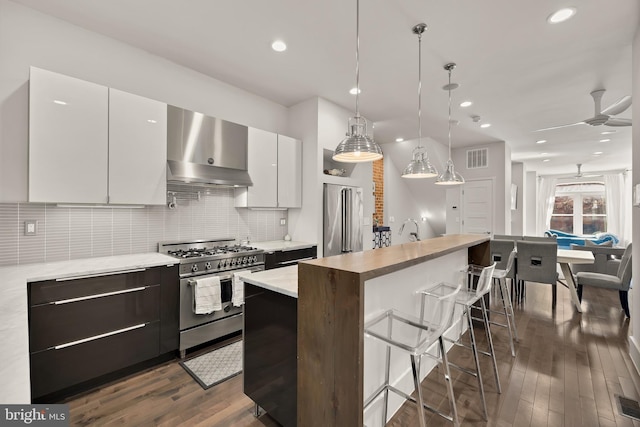 kitchen with tasteful backsplash, dark wood finished floors, premium appliances, a kitchen breakfast bar, and wall chimney range hood