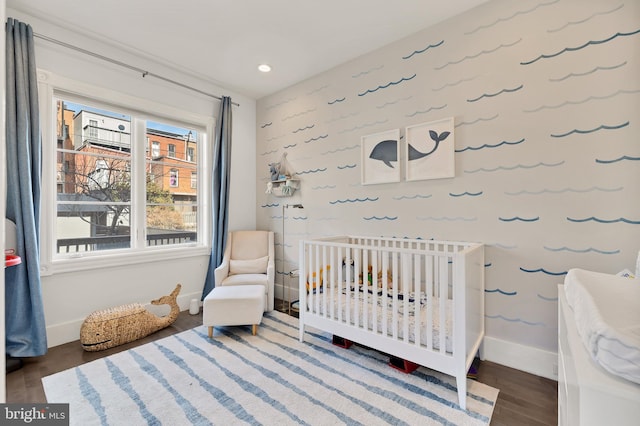 bedroom featuring recessed lighting, a crib, baseboards, and wood finished floors