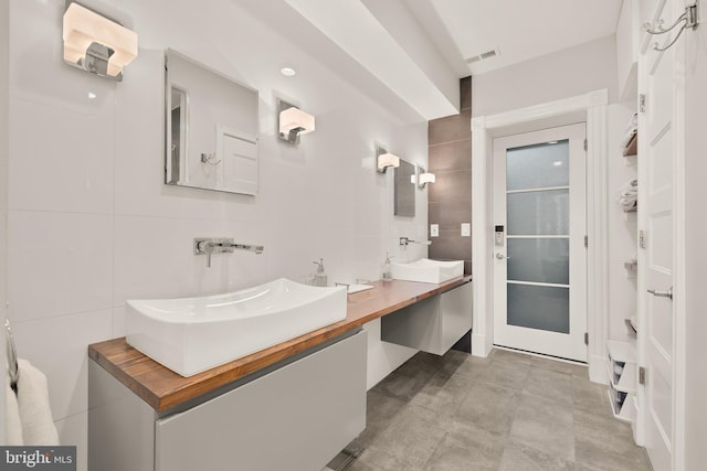 full bathroom with a sink, visible vents, tile walls, double vanity, and tasteful backsplash