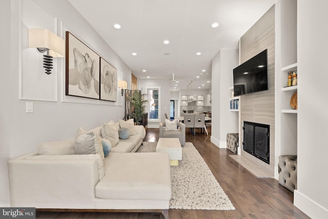 living room featuring a large fireplace, dark wood-style flooring, baseboards, and recessed lighting