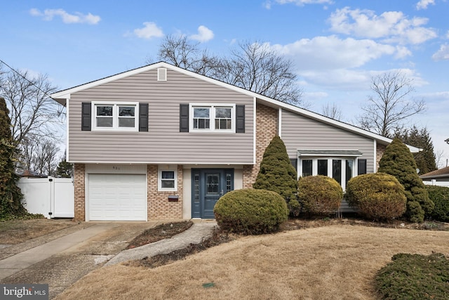 tri-level home featuring a garage, brick siding, driveway, and fence