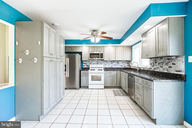 kitchen with light tile patterned floors, a ceiling fan, appliances with stainless steel finishes, a sink, and backsplash