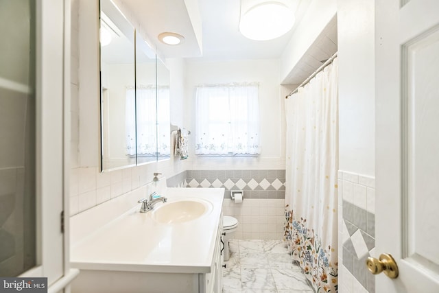 full bathroom featuring toilet, a wainscoted wall, marble finish floor, vanity, and tile walls