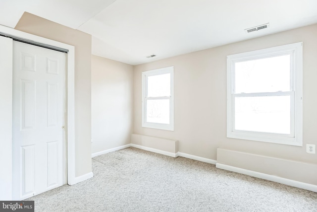 empty room with carpet, visible vents, and baseboards