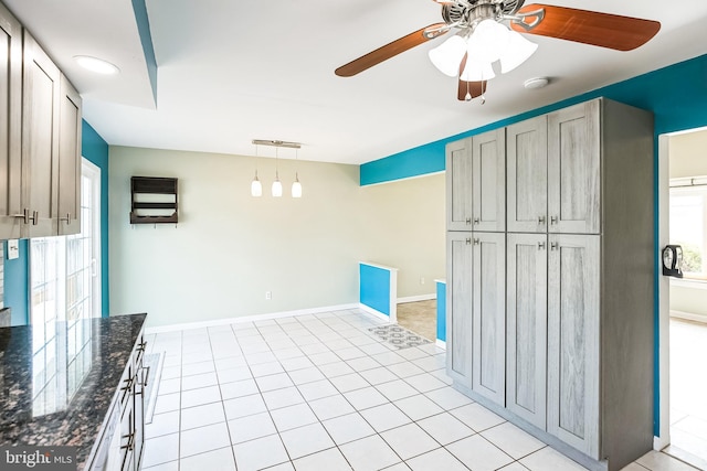 kitchen with baseboards, dark stone counters, ceiling fan, hanging light fixtures, and light tile patterned flooring