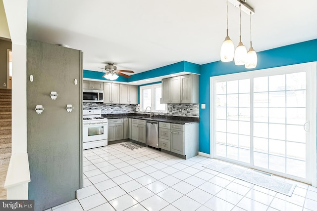 kitchen with gray cabinetry, stainless steel appliances, a sink, decorative backsplash, and dark countertops