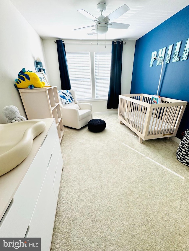 carpeted bedroom featuring a nursery area and ceiling fan