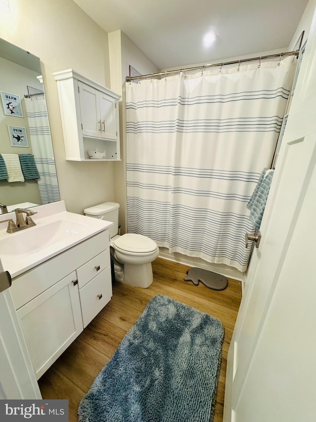 bathroom featuring toilet, shower / tub combo, wood finished floors, and vanity