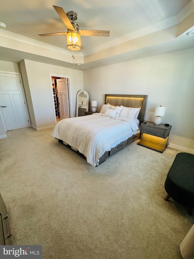 bedroom with baseboards, a ceiling fan, a spacious closet, a tray ceiling, and carpet floors