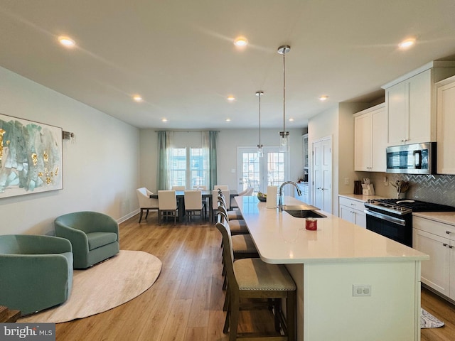 kitchen with an island with sink, gas range, stainless steel microwave, a sink, and backsplash