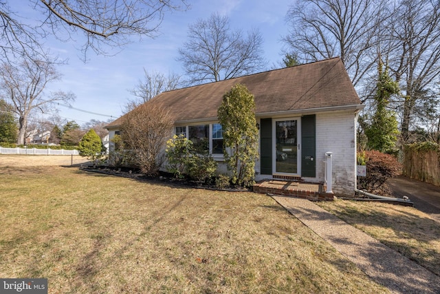 view of front facade featuring brick siding, roof with shingles, a front yard, and fence