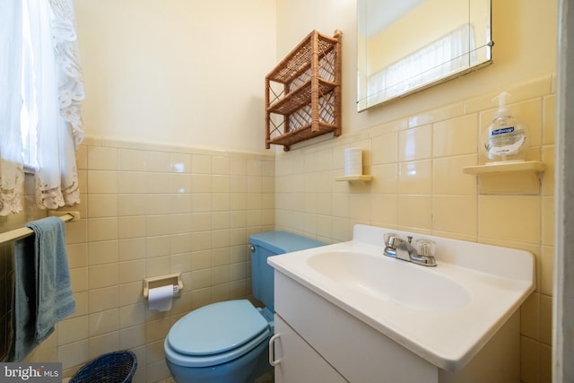 half bathroom with vanity, tile walls, toilet, and a wainscoted wall