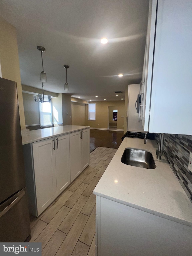 kitchen with wood finish floors, light countertops, hanging light fixtures, freestanding refrigerator, and white cabinetry