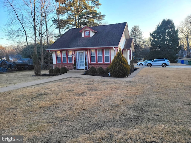 view of front of property with roof with shingles, a front yard, and brick siding