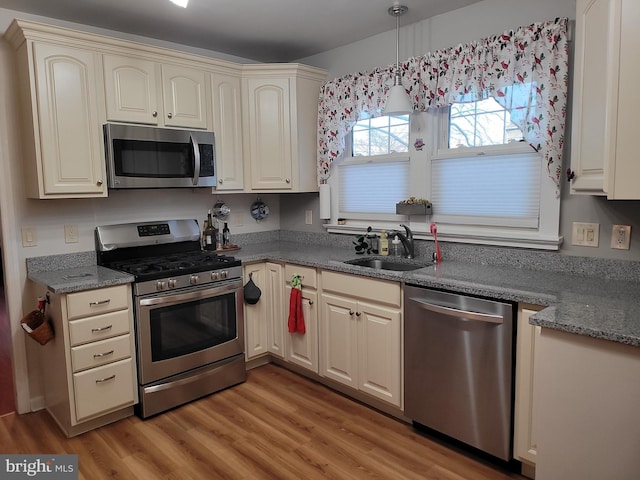 kitchen with pendant lighting, cream cabinets, appliances with stainless steel finishes, a sink, and light wood-type flooring