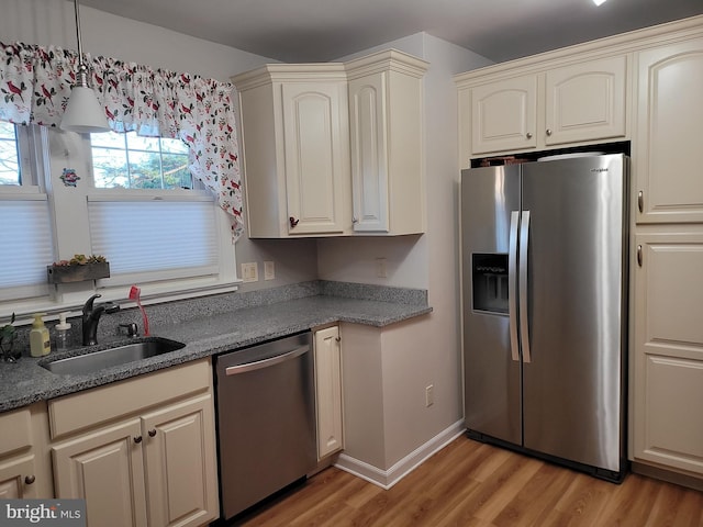 kitchen with light wood finished floors, baseboards, appliances with stainless steel finishes, stone counters, and a sink