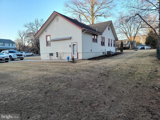 view of home's exterior featuring central AC, a lawn, a chimney, and roof with shingles