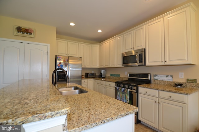 kitchen featuring stainless steel appliances, recessed lighting, white cabinetry, a sink, and light stone countertops