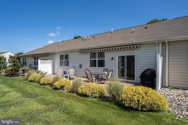 rear view of property with a shingled roof, a yard, and a patio