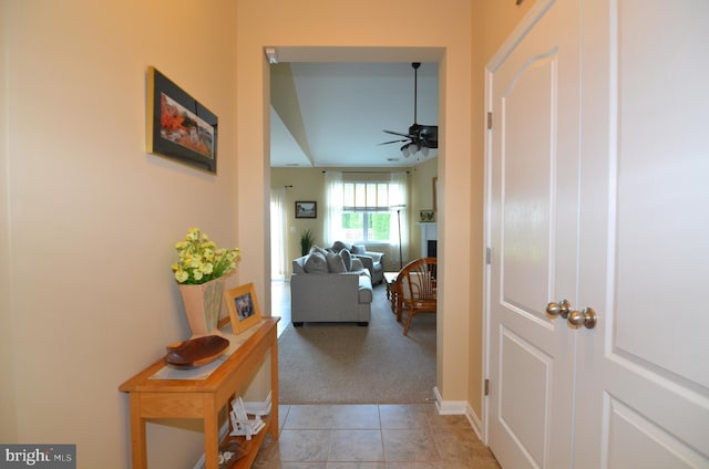 corridor featuring light tile patterned floors, baseboards, and light colored carpet