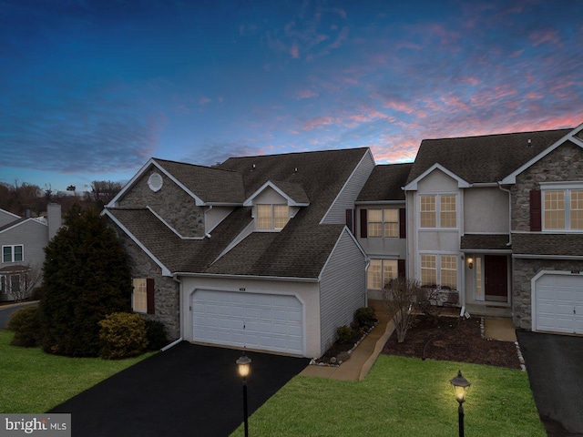 traditional home with aphalt driveway, a front yard, stone siding, and a garage