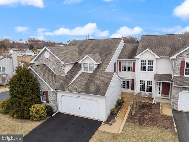 view of front of home featuring stone siding, roof with shingles, and driveway