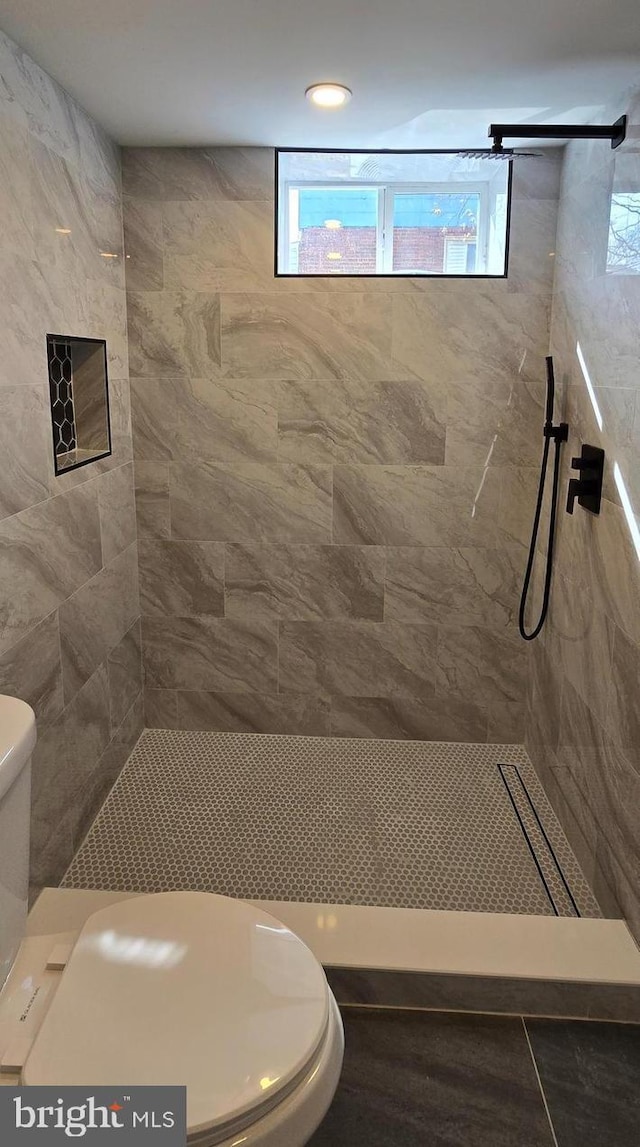 full bathroom featuring a wealth of natural light, a tile shower, and toilet